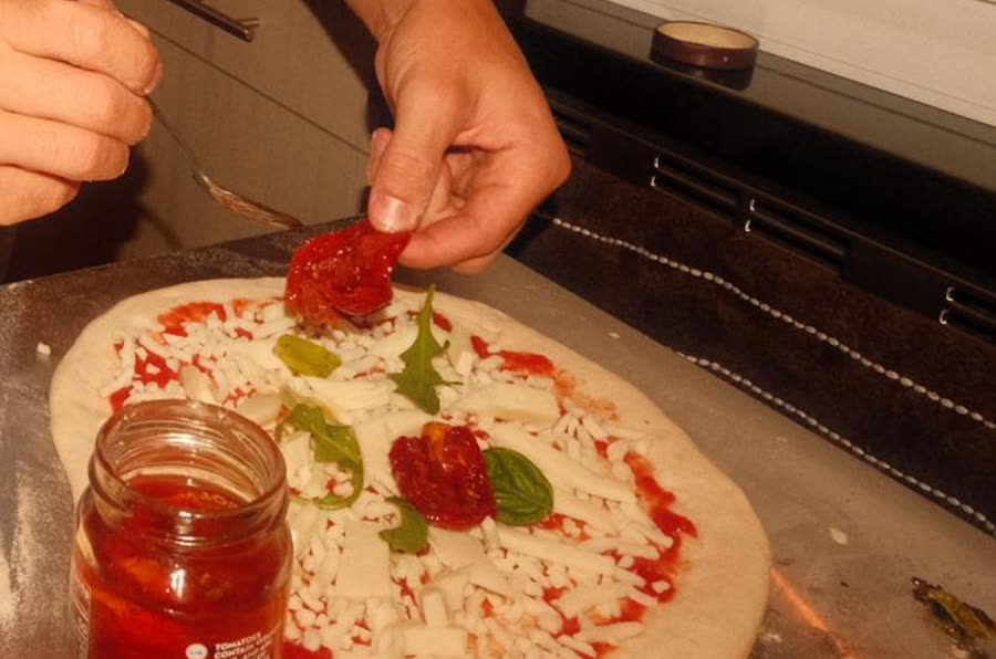 Close-up of hands placing sun-dried tomatoes and basil on a pizza